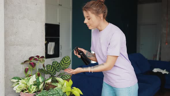 Young Blonde Lady Taking Care About Her Domestic Plants Spraying Flowers in Pots at Home