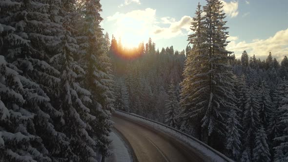 Aerial view of winter landscape with snow covered mountain hills and winding forest road in morning.