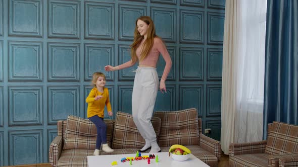 Happy Funny Family Mother and Child Kid Daughter Dancing Jumping on Sofa Listening Music at Home