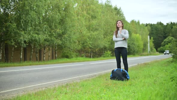 Young woman waiting for transport on the side of the road with a travel bag