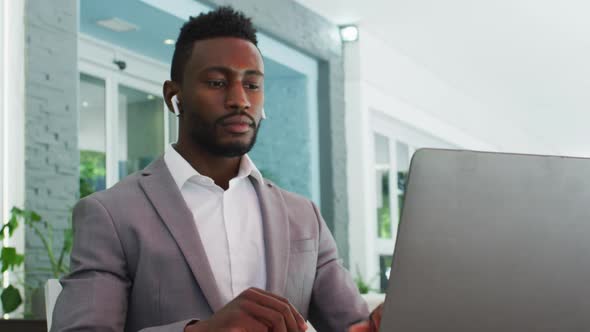 African american businessman using wireless earphones and laptop in cafe