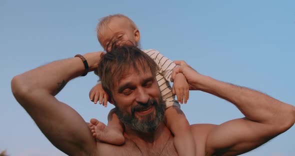 Smiling Baby Boy Sits on Fathers Neck and Have Fun Together Outdoor in Sunset