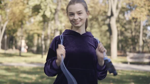 Middle Shot of Joyful Beautiful Young Sportswoman Standing with Jumping Rope in Sunlight and Smiling