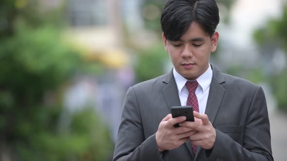 Young Handsome Asian Businessman Using Phone in the Streets Outdoors