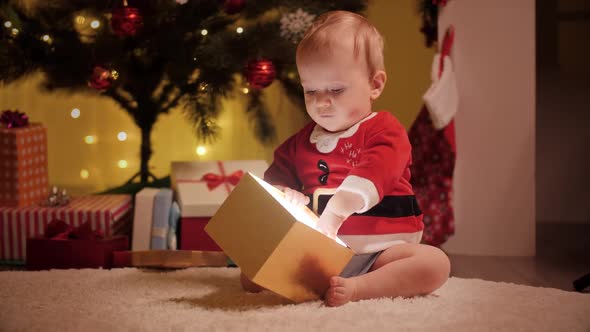 Cute Baby Boy in Santa Costume Looking Inside Christmas Present Box