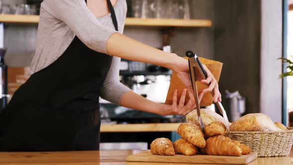 Mid-section of waitress packing croissants in paper bag