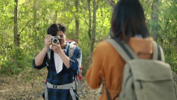 A boyfriend taking a photo of a girlfriend in the forest on sunny beautiful summer.