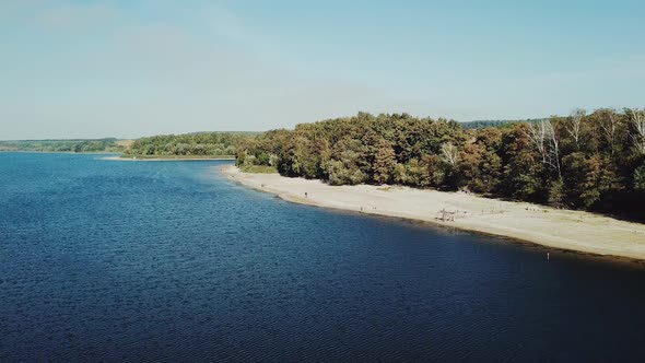 A beautiful resting place with a wide river and a sandy beach near green and long fields.