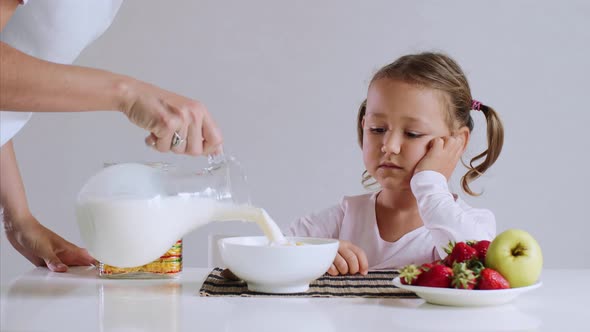 Sleepy girl is starting to eat her cornflakes with milk for breakfast.