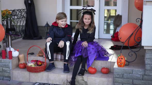 Wide Shot Two Happy Kids Singing and Dancing Sitting on Front Yard Porch on Halloween