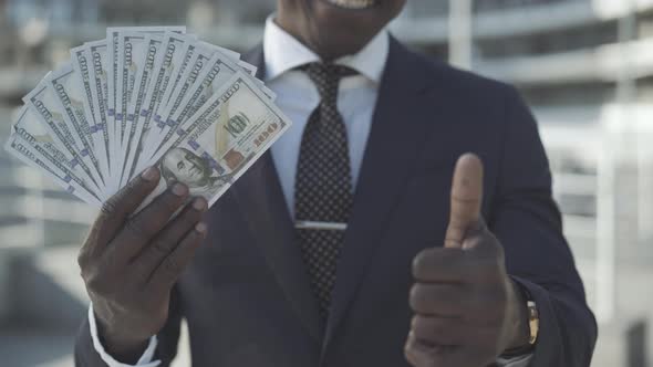 Unrecognizable African American Man Holding Dollars and Showing Thumb Up at Camera. Happy Successful