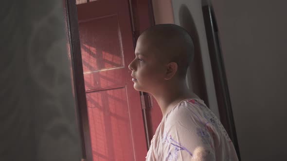 Bald Indian girl looking outside from window at home due to covid-19 lockdown and quarantine