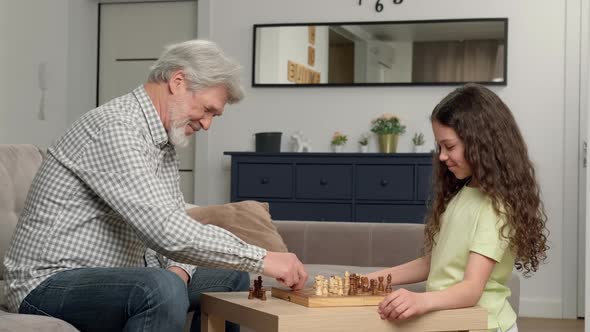 Grandfather Teaches Granddaughter to Play Chess at Home in the Living Room