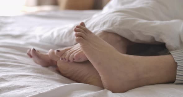 Side View Close-up of Unrecognizable Male and Female Feet Moving and Hiding Under White Blanket