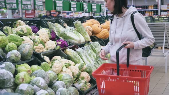 A Young Woman in a Supermarket Holds Fresh Organic Vegetables in Her Hands and Puts Green Cabbage in