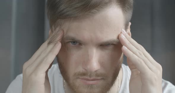 Extreme Close-up of Brunette Caucasian Man with Grey Eyes Rubbing Temples