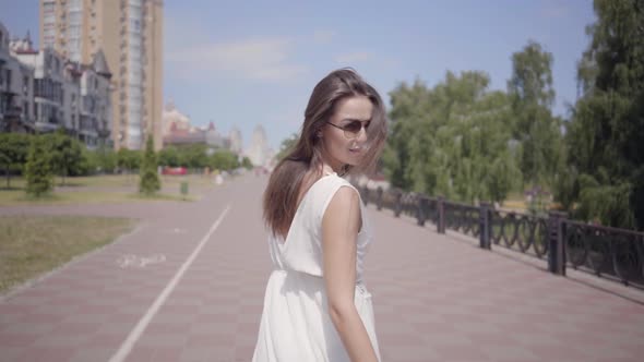 Glamorous Young Girl Wearing Sunglasses and a Long White Summer Fashion Dress Walking