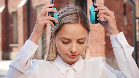 Pretty Blonde Women Wears Headphones Listening to Music Looking in Camera