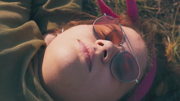 Young Woman in Orange Sunglasses Sleeps on Brown Meadow