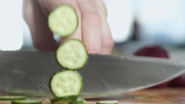 chef in modern kitchen cuts fresh cucumber for salad.