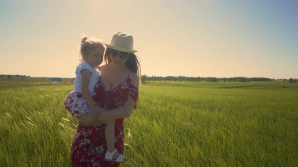 Closeup Tracking Mom Wearing Summer Dress Sunglasses Walks Across Endless Field Holding Little