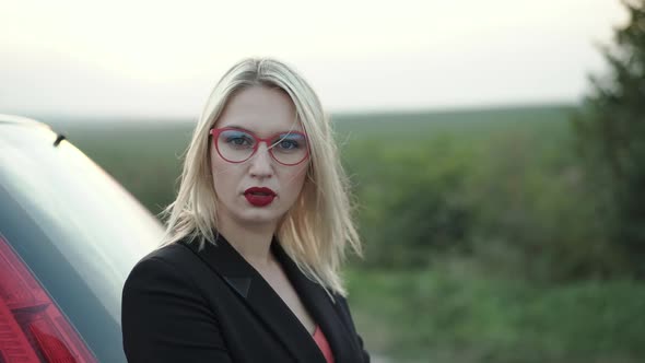 Portrait of Confident Blonde with Blowing Hair Looks Into Camera at Suburban Way