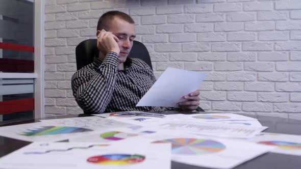 Young Man Talking On The Phone And Working With Graphs