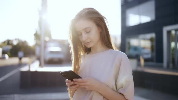 Young Woman in a Bright Sunlight Uses Phone