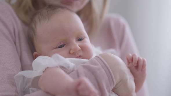 Closeup Cute Thoughtful Baby Girl in Hands of Unrecognizable Caucasian Woman