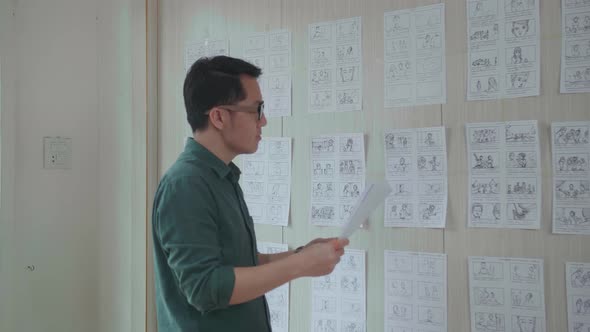 Young Creative Asian Designer Looks At The Storyboard Sketches Covering His Wall