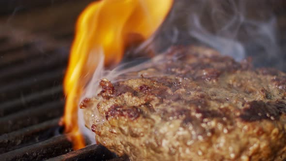 Slow motion of beef hamburger on a grill in close up with flames and smoke