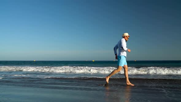 Happy Man Runs Along the Ocean Beach at Sunset