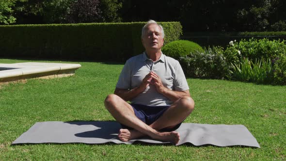 Caucasian senior man practicing yoga meditating in garden in the sun