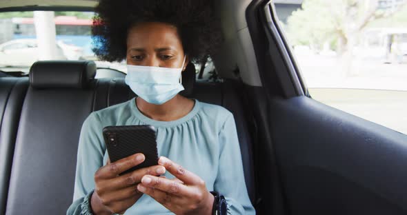 African american businesswoman with face mask using smartphone