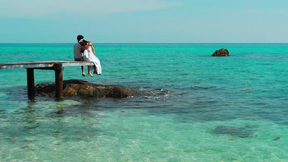 happy young couple sitting on wood bridge and sea beach at Koh MunNork Island, Rayong, Thailand