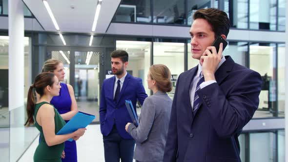 Businessman discussing with colleague while talking on mobile phone