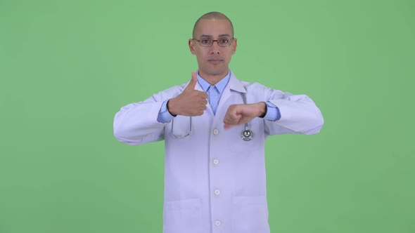 Confused Bald Multi Ethnic Man Doctor Choosing Between Thumbs Up and Thumbs Down