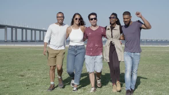 Group of Smiling Friends Hugging While Strolling on Meadow