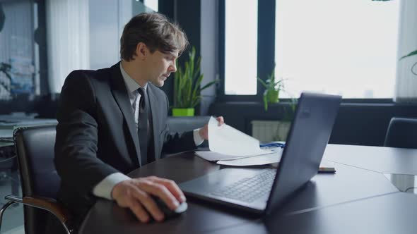 Portrait of Confident Handsome Brunette Male Employee Sitting in Office Analyzing Documents Typing