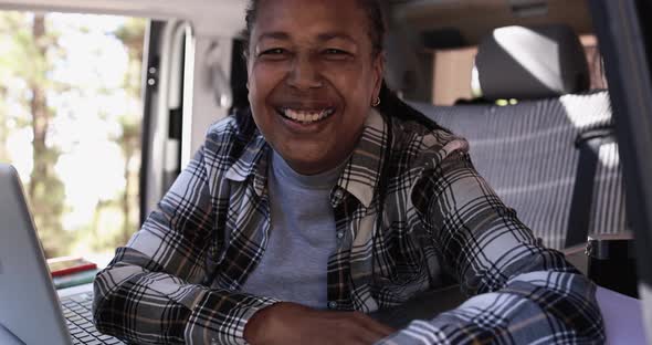 Mature african woman sitting inside mini van camper and smiling on camera