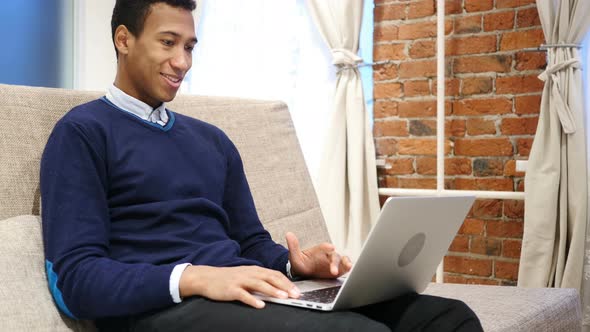 African Man Doing Video Chat on Laptop, Sitting on Sofa at Home