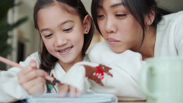 Positive Asian girl writing in notepad and her mother kissing her