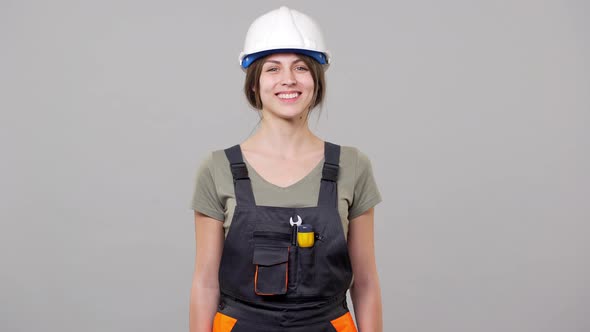 Portrait of Caucasian Young Woman Builder in Helmet and Jumpsuit Smiling and Nodding While Working