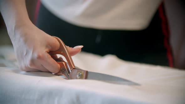 Young Woman Seamstress Cutting the Cloth with Big Scissors