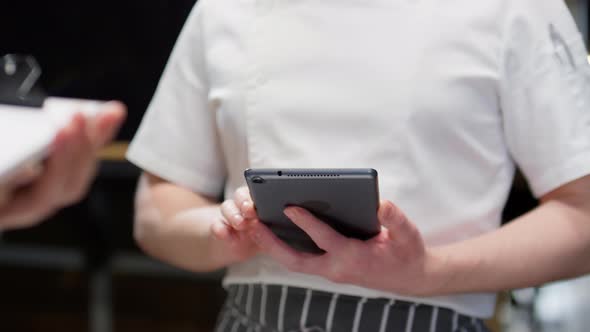 Chef Using Tablet and Speaking with Colleague in Restaurant Kitchen