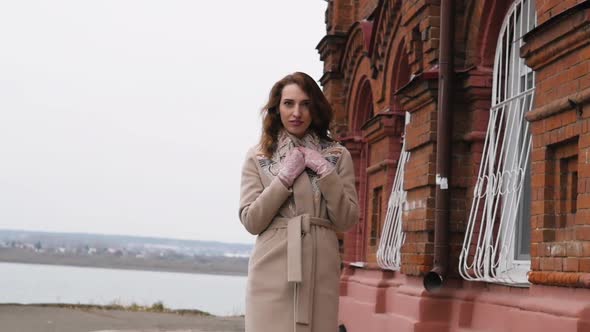 Young Redhaired Woman in a White Coat Walks on the Background of the Old City