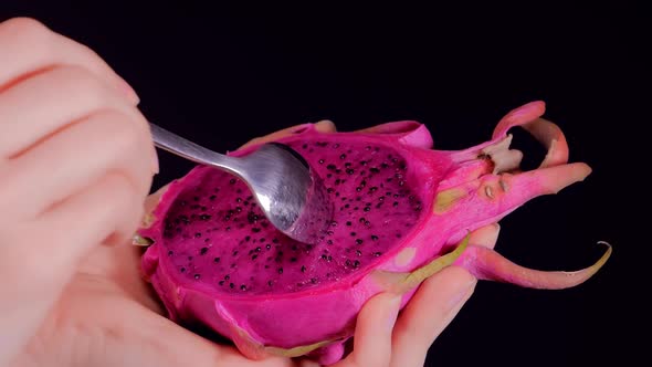 Dragon Fruit or Pitaya with a Spoon in Female Hands on Black Background