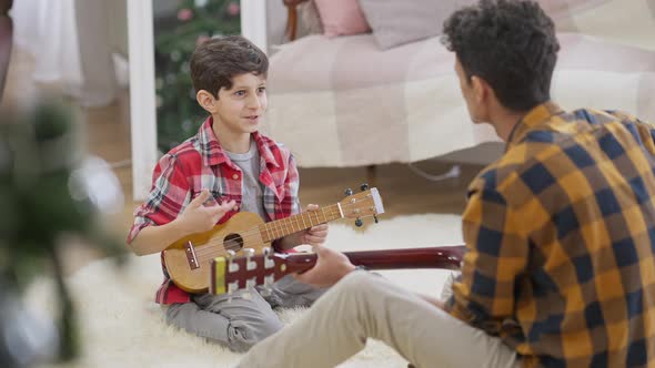 Wide Shot Portrait of Happy Smiling Middle Eastern Boy Playing Ukulele with Brother Playing Guitar