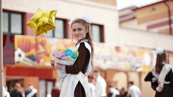 Happy Girl Graduate with Yellow Balloon and Flowers Posing on Graduation Day