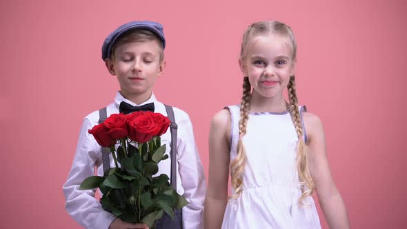 Smiling Girl and Her Little Boyfriend Holding Red Flowers, Looking to Camera